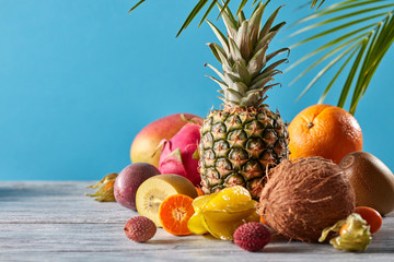 Creative exotic composition with tropical fruits and green leaves pineapple, coconut, mango, kiwi, pitahaya on a wooden table on a blue.