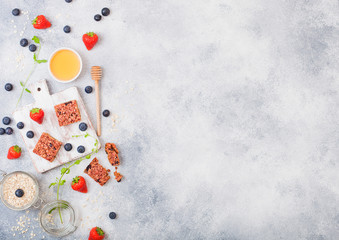 Organic cereal granola bar with berries on vintage board with honey spoon and jar of oats on marble background. Strawberry, raspberry and blueberry with mint leaf and bowl of honey