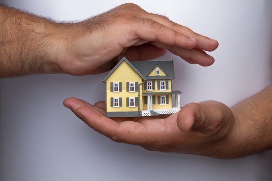 Human Hands Holding and Protecting a Model of a House on Grey