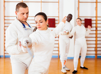 Woman fencer practicing new movements with trainer  at fencing room