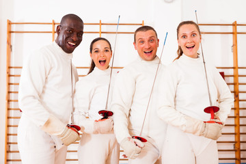 Positive fencers standing with foils  together at fencing workout