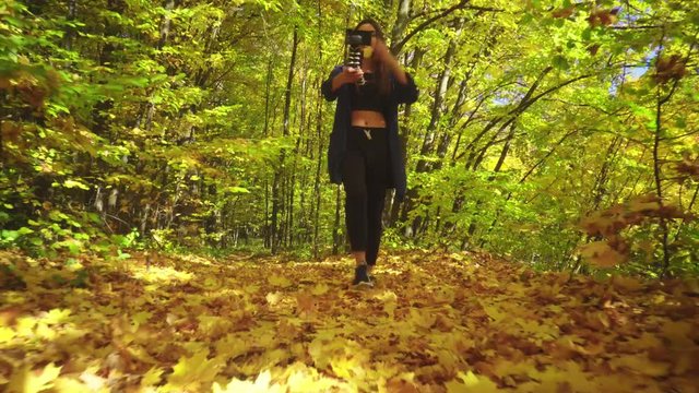 Blogger charismatic young woman is walking in autumn forest and recording video for vlog using camera talking actively gesturing and smiling