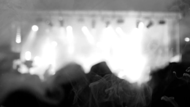 Blurred scene of a rock concert with musicians on stage and the crowd in the shadow. Bright lighting, contrasted black and white scene. A smoke covers the screen.