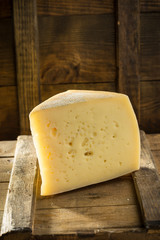 Slice of asolo cheese on wooden board on dark background