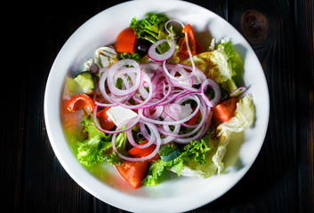 Appetizing fresh vegetable salad with spicy sauce in a white plate on a dark table