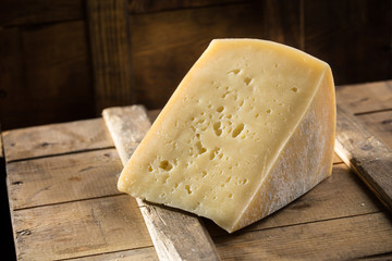 Slice of asolo cheese on wooden board on dark background