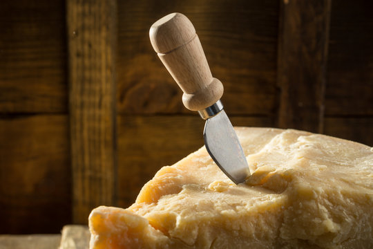 Parmesan cheese with knife on wooden board on dark background