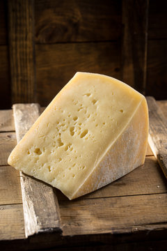 Slice of asolo cheese on wooden board on dark background