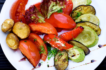Grilled vegetables in a white plate and with sauce. Tomatoes, mushrooms, zucchini, pepper, eggplant.