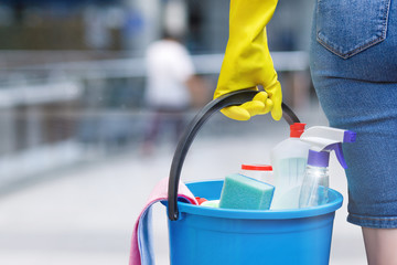 A woman carrying a bucket fulfiled with the chemical staff in her hand in rubber glove.