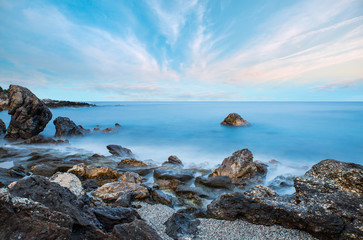 Long exposure image of dramatic sky with rock in sunset