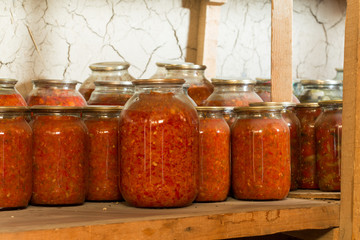 Preserved food in glass jars, on a wooden shelf. Various marinaded food