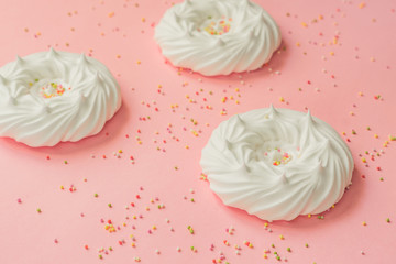 homemade white air meringues and confectionery decorations on pink background