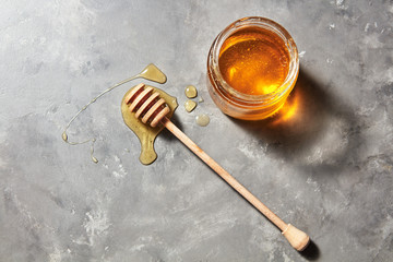 Sweet flower natural honey in a jar and wooden spoon on a gray concrete table. Top view. Jewish New...