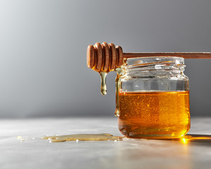 Dripping organic natural fresh honey from glass pot on a gray kitchen table. Rosh hashanah jewish...