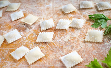 traditional white uncooked ravioli with cheese on a cutting board with flour, handmade, on a wooden table. cooking process