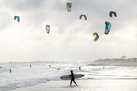 un surfer passe devant des kitesurf sous un ciel nuageux