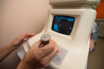 The doctor's hands control the apparatus for testing the vision behind which the patient is sitting