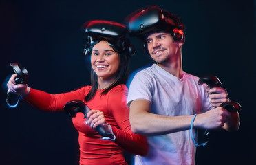 Young smiling couple having fun together, play with VR headsets and controllers.