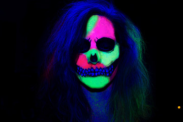 Woman with her face painted with neon make up with a skull design for halloween and santa muerte