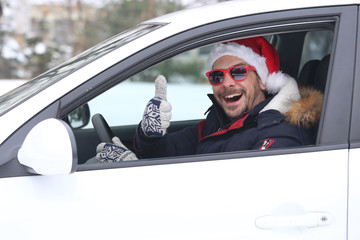Close up portrait of car driver with santa hat and thumb up enjoying the snow and sunny dan.