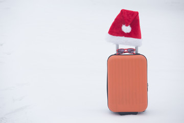 Orange suitcase with sunglasses and santa hat on snow. Copy space