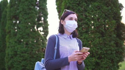 Girl in a protective medical mask on her face goes and uses the phone
