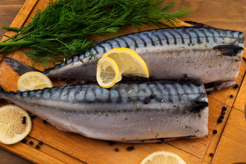 Thawed mackerel in a marinade of black pepper, lemon and dill on a wooden background.