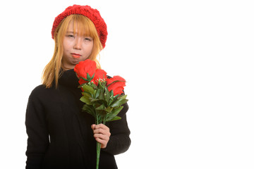 Young cute Asian woman holding red roses looking upset