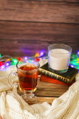 Cozy winter still life: cup of hot tea and books, candle on wooden background and blurred garland lights