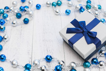 closeup Christmas gift with blue ribbon and silver and blue Christmas balls on white wooden background