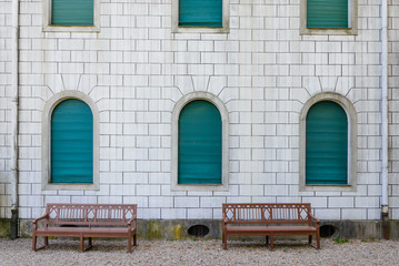 Fototapeta na wymiar Exterior facade white stone wall, arch green windows and wooden bench.
