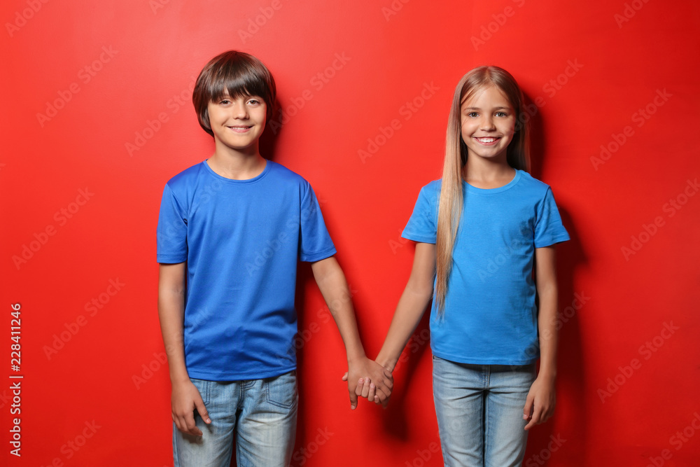 Wall mural Boy and girl in t-shirts holding hands on color background