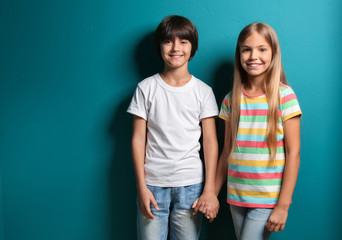 Smiling boy and girl in t-shirts holding hands on color background © Pixel-Shot