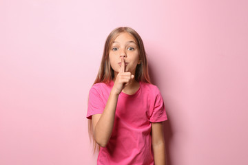 Little girl in t-shirt showing silence gesture on color background