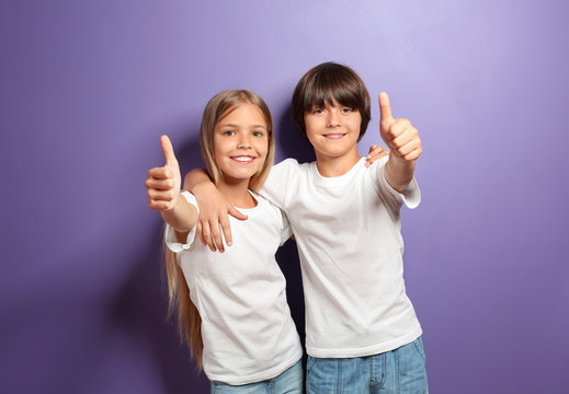 Hugging boy and girl in t-shirts showing thumb-up on color background