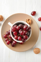 Cup with sweet grapes on white wooden table
