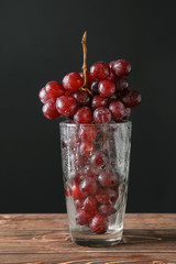 Glass with grapes on table against dark background