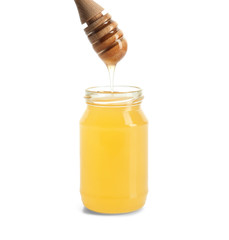 Honey dripping from dipper into jar on white background