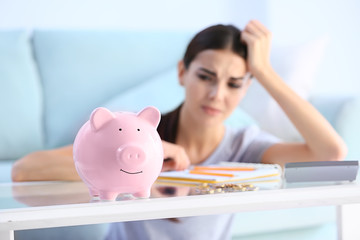 Piggy bank on table of young upset woman