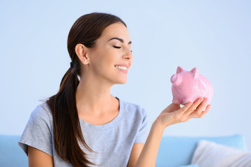 Beautiful young woman with piggy bank at home