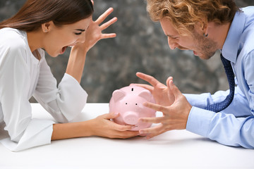 Young quarreling couple with piggy bank at table