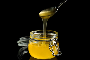 Honey pouring from metal spoon in glass jar against dark background