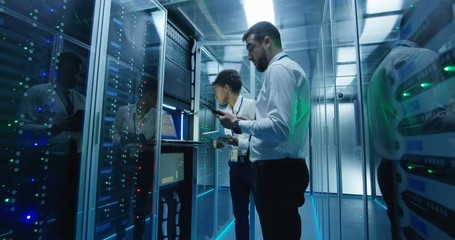 Side view of multiethnic man and woman with tablet diagnosing server hardware opening glass door of rack in data center corridor