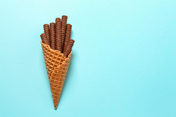 Waffle cone with chocolate wafer sticks on color background