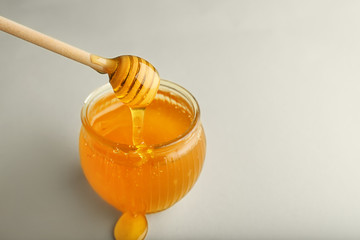 Glass jar with honey and dipper on light background