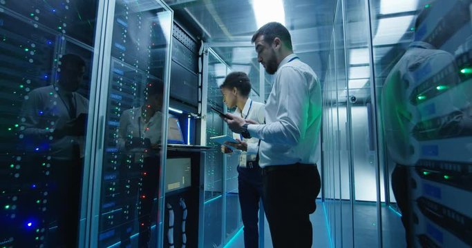 Side view of multiethnic man and woman with tablet diagnosing server hardware opening glass door of rack in data center corridor