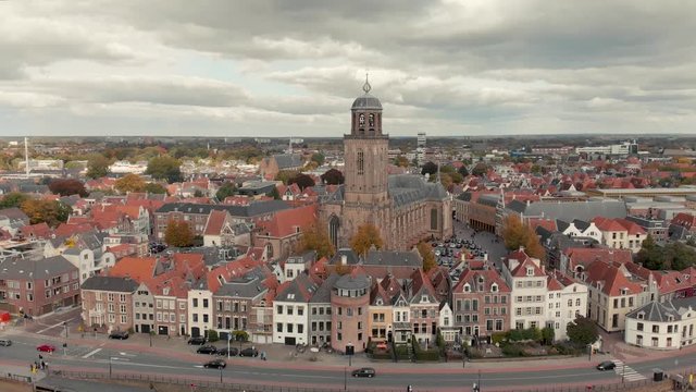 Aerial drone shot starting high up and slowly descending showing the Dutch medieval city of Deventer revealing the boulevard with traffic at the river IJssel that passes by on a cloudy day