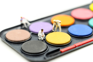 Miniature people : worker painting with watercolor paints and paintbrushes for painting.