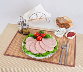 Sliced boiled sausages with tomatoes on lettuce leaves are laid on a plate.
